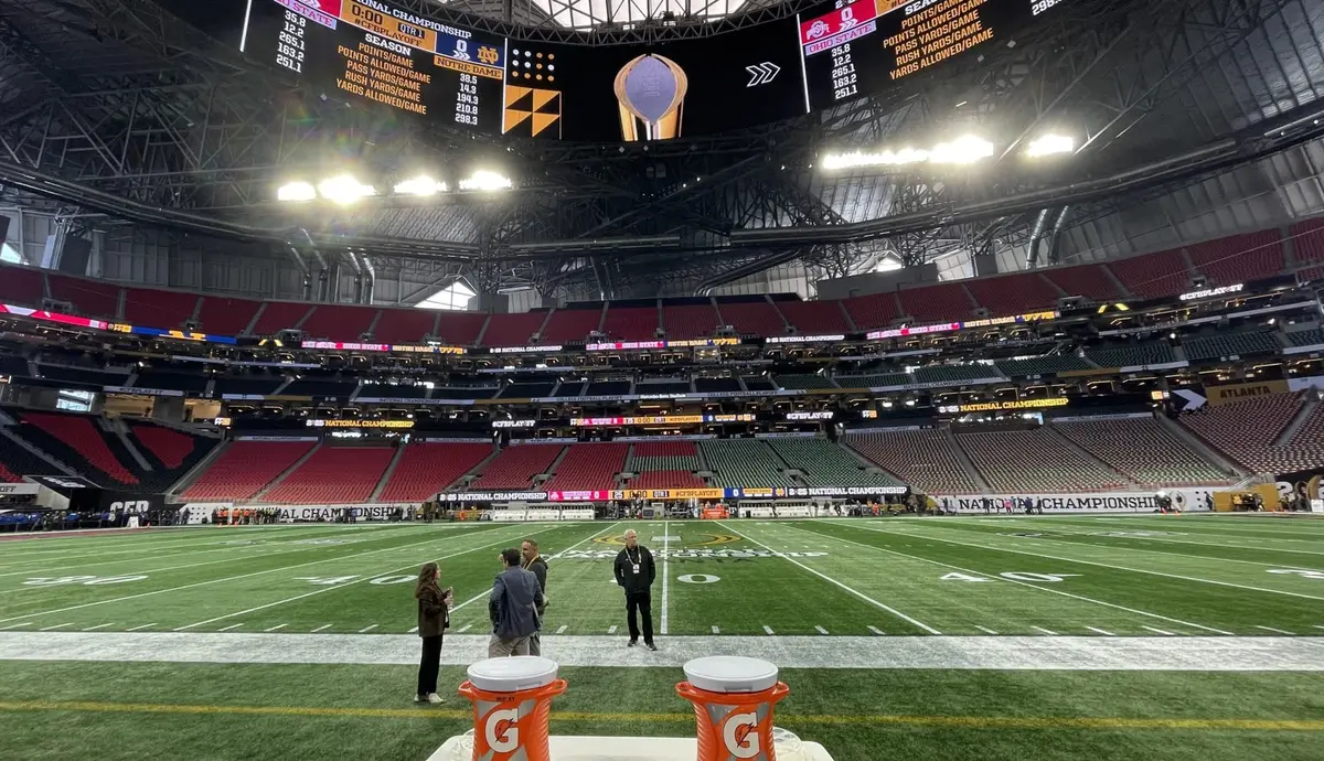 An empty Mercedes-Benz Stadium seen from field level, dressed for the national championship, the scoreboard showing Ohio State and Notre Dame season numbers