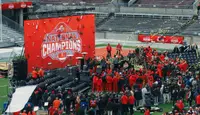 Ohio State players in scarlet gathered on a stage on the Ohio Stadium field beside a National Champions screen, gold streamers in the air and fans crowded on the turf around them