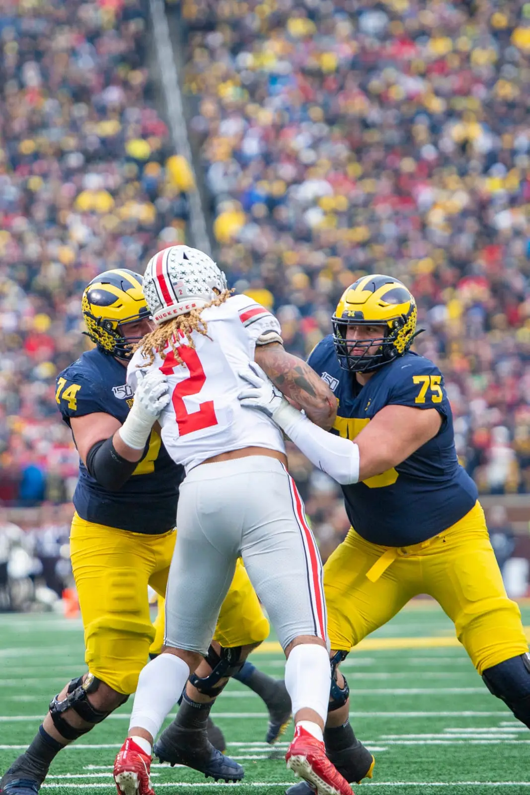 Ohio State defensive end Chase Young, number 2 in road white, driving between two Michigan offensive linemen, numbers 74 and 75