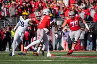 Ohio State quarterback C.J. Stroud steps up in the pocket in a scarlet jersey as a Michigan pass rusher closes from the left and two Buckeye linemen block