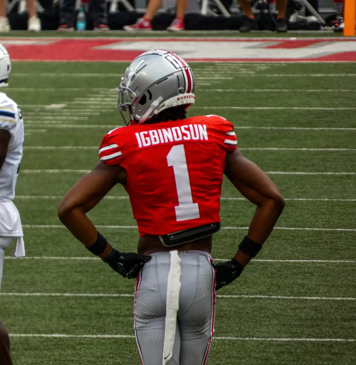 Ohio State cornerback Davison Igbinosun, number 1 in a scarlet jersey with his name across the shoulders, standing with his hands on his hips on the field