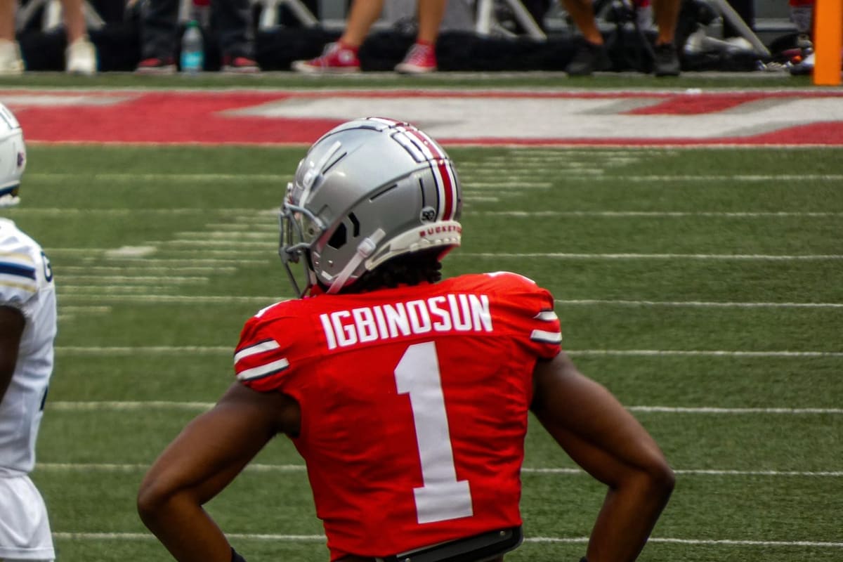 Ohio State cornerback Davison Igbinosun, number 1 in a scarlet jersey with his name across the shoulders, standing with his hands on his hips on the field