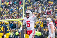 Garrett Wilson in a white number 5 Ohio State road jersey raising one arm in a packed Michigan Stadium