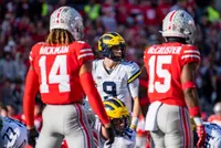 Ohio State safeties Ronnie Hickman, number 14, and Tanner McCalister, number 15, seen from behind in scarlet jerseys, facing the Michigan quarterback before a snap