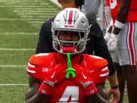 Jeremiah Smith in a scarlet number 4 Ohio State jersey and silver helmet on the sideline, holding his mouthguard strap with both hands