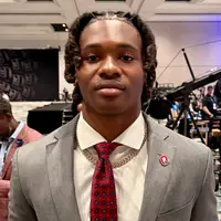 Ohio State receiver Jeremiah Smith in a grey suit and a scarlet patterned tie, a Block O pin on his lapel, standing in front of television cameras