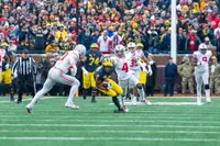 Ohio State safety Jordan Fuller, number 4 in road white, closing on a Michigan ball carrier in the open field, teammates and a Michigan lineman behind them