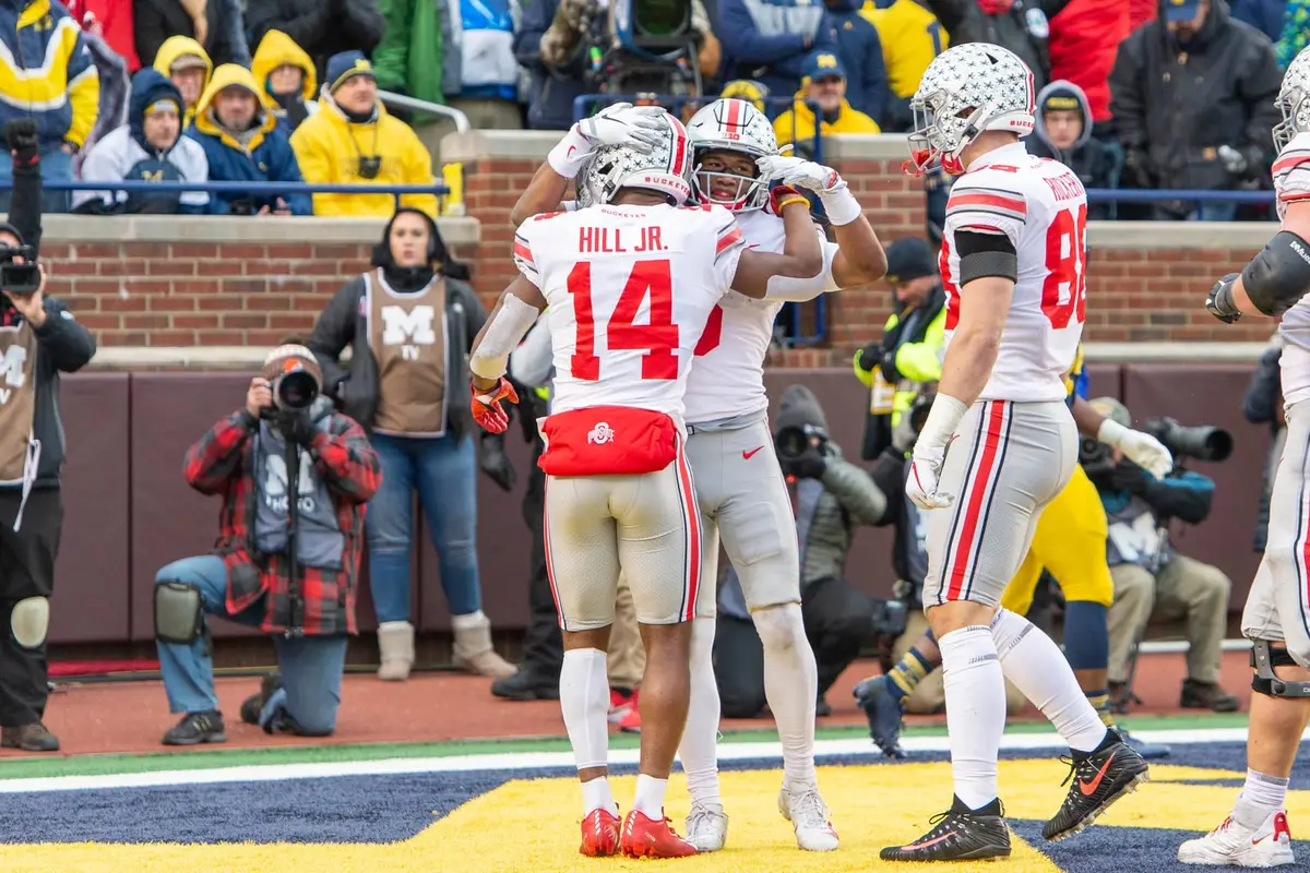 Ohio State receiver K.J. Hill Jr., his name and number 14 on the back of a white road jersey, being hugged by teammates in the end zone