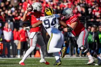 An Ohio State offensive lineman in scarlet locking up Michigan defensive tackle number 94 as quarterback C.J. Stroud cocks his arm to throw behind him