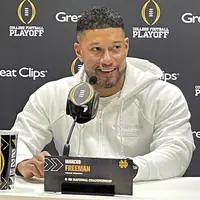 Marcus Freeman in a white Notre Dame hoodie at a College Football Playoff podium, behind a nameplate reading Marcus Freeman, Head Coach