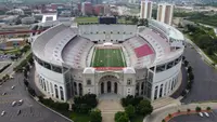 An aerial view of Ohio Stadium, the horseshoe open toward the camera with its rotunda entrance in front, the empty field inside and the Ohio State campus beyond