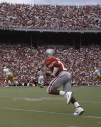An Ohio State player in scarlet running downfield alone in a packed Ohio Stadium as Colorado players in white spread across the field