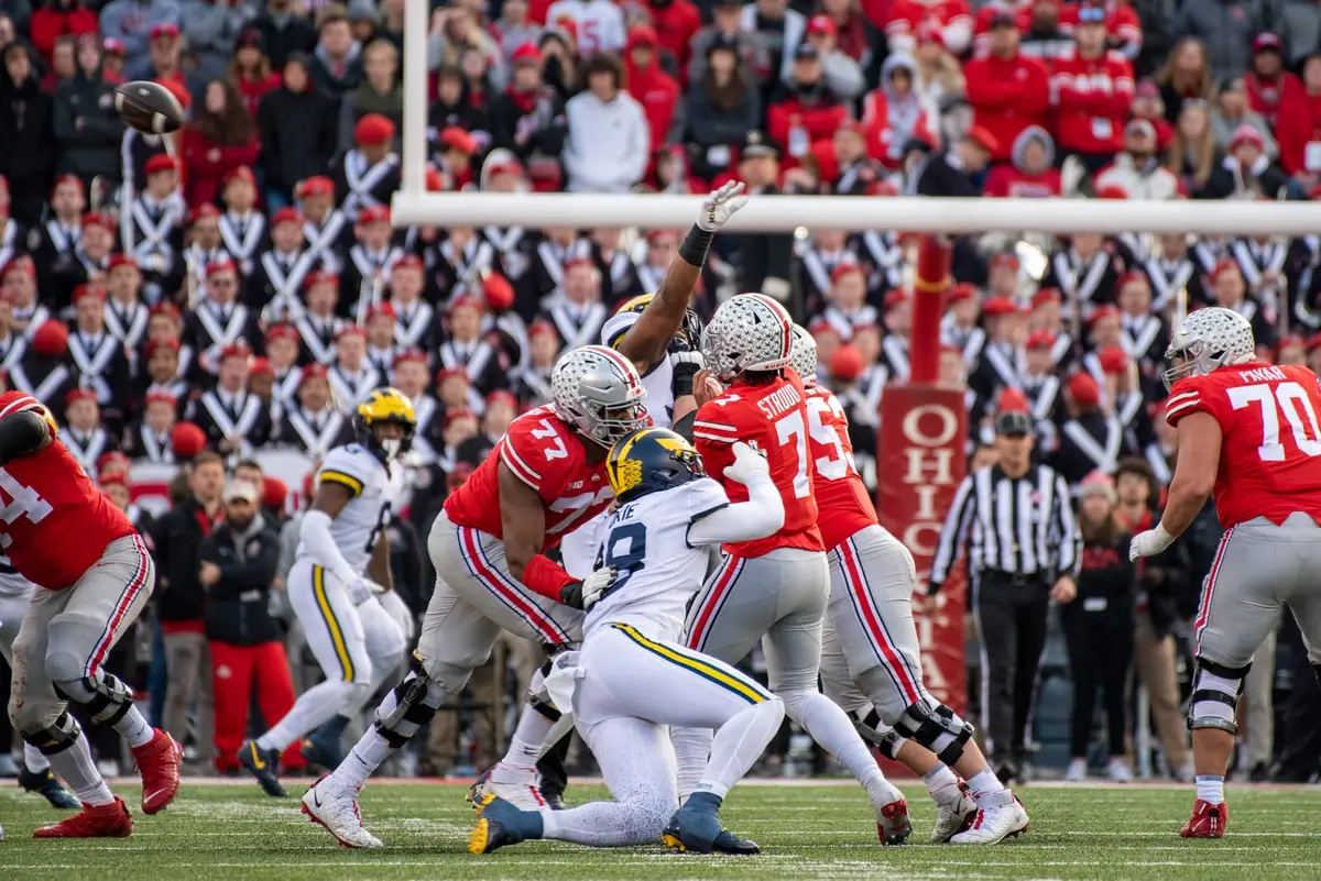 Ohio State linemen in scarlet blocking Michigan defenders at the line of scrimmage, the ball in the air above the goalpost