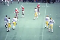Ohio State players in scarlet and Michigan players in white and yellow walking between plays on the field at Ohio Stadium, photographed from high in the stands