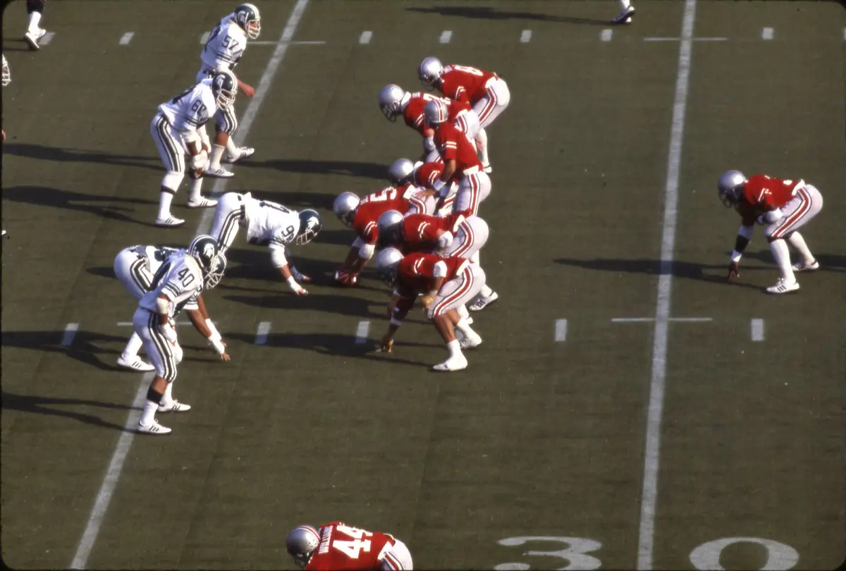 Ohio State players in scarlet lined up at the line of scrimmage against Michigan State players in white at Ohio Stadium