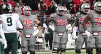 Ohio State offensive linemen in grey uniforms on the field with a Michigan State player at left