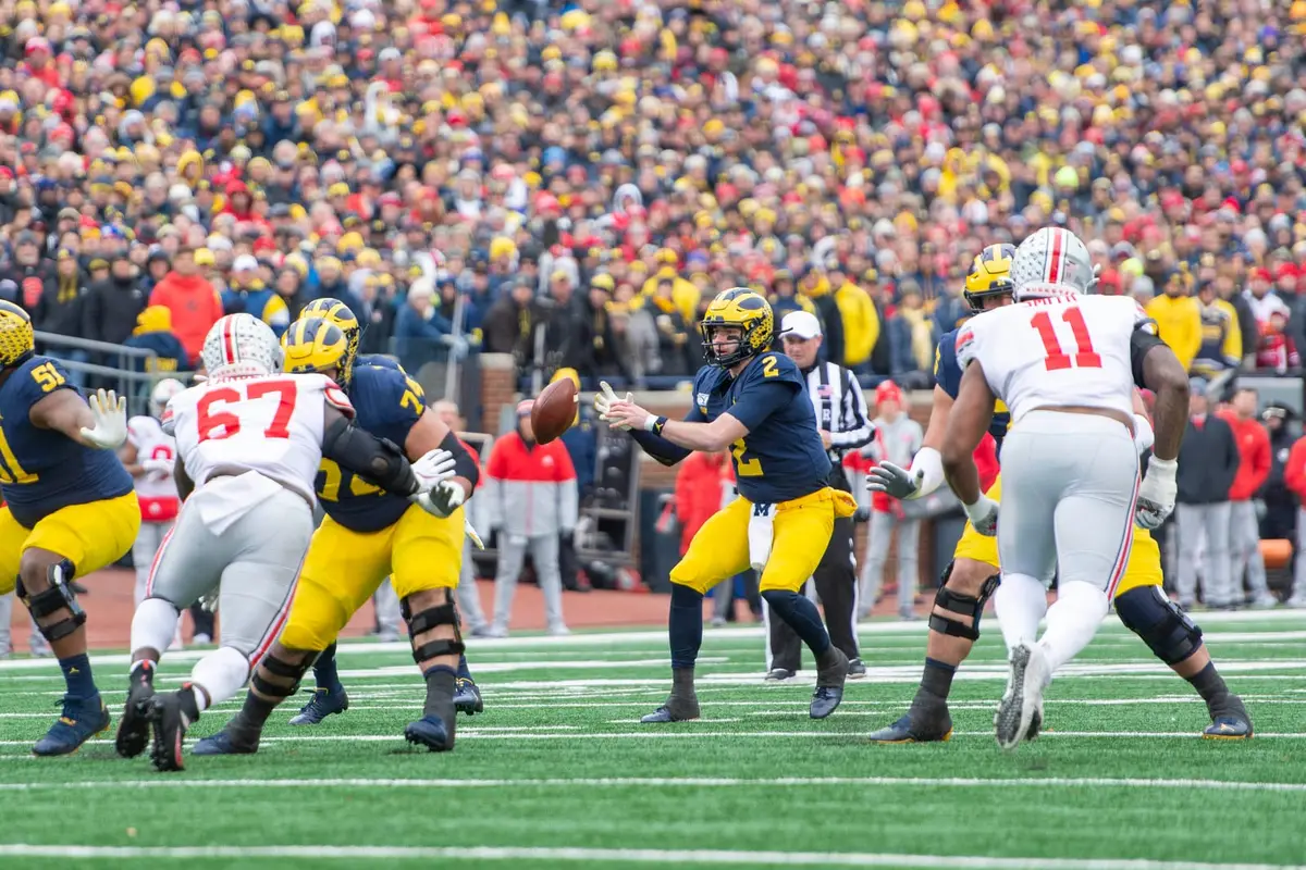 Ohio State defenders in road white, numbers 67 and 11 among them, rushing the Michigan quarterback as he sets to throw