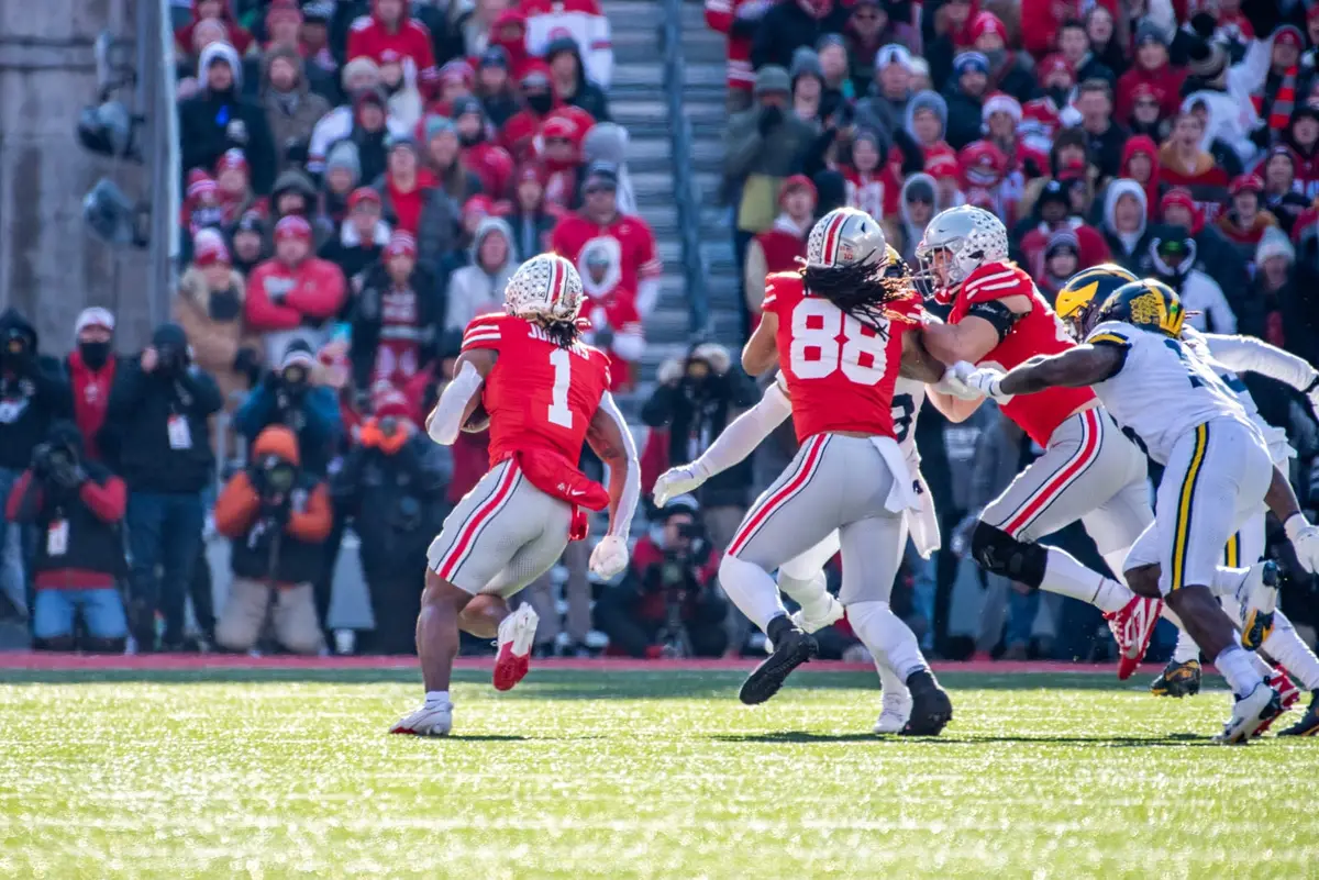 Ohio State running back Quinshon Judkins, number 1 with his name across the shoulders, carrying the ball away from the camera as number 88 and a lineman block Michigan defenders