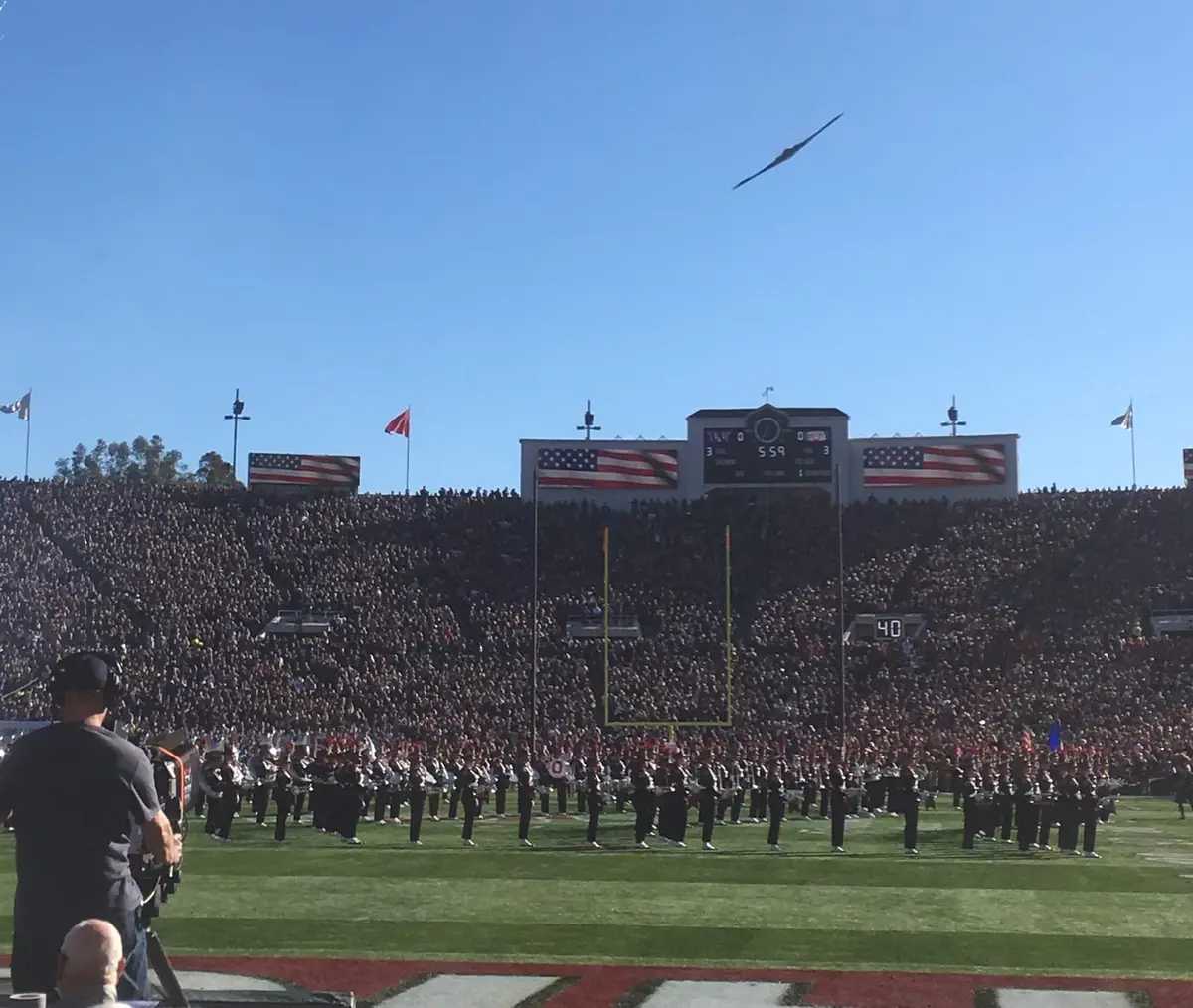 A B-2 bomber flies over the Rose Bowl as the marching bands stand on the field