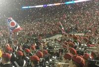 Red and white confetti falling over Ohio State Marching Band trumpet players in red berets, an Ohio flag waving above them and a packed stand behind