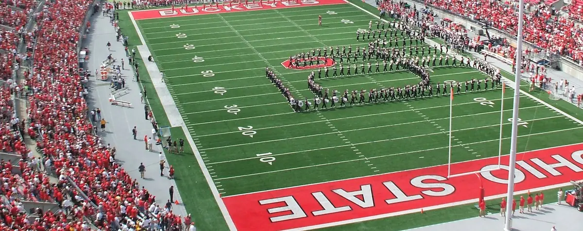 The Ohio State University Marching Band spelling out Script Ohio in white across the green field at Ohio Stadium, between the scarlet BUCKEYES and OHIO STATE end zones