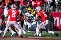 Ohio State linebacker Sonny Styles, number 6 with his name across the shoulders, driving into a Michigan blocker while safety Caleb Downs, number 2, closes on the Michigan ball carrier