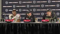 Cody Simon, Ryan Day and Will Howard seated behind nameplates at a National Championship press conference table with two trophies