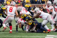 Ohio State running back TreVeyon Henderson, his name across the back of his white jersey, driving low into a pile of Michigan defenders as Ohio State blockers push behind him
