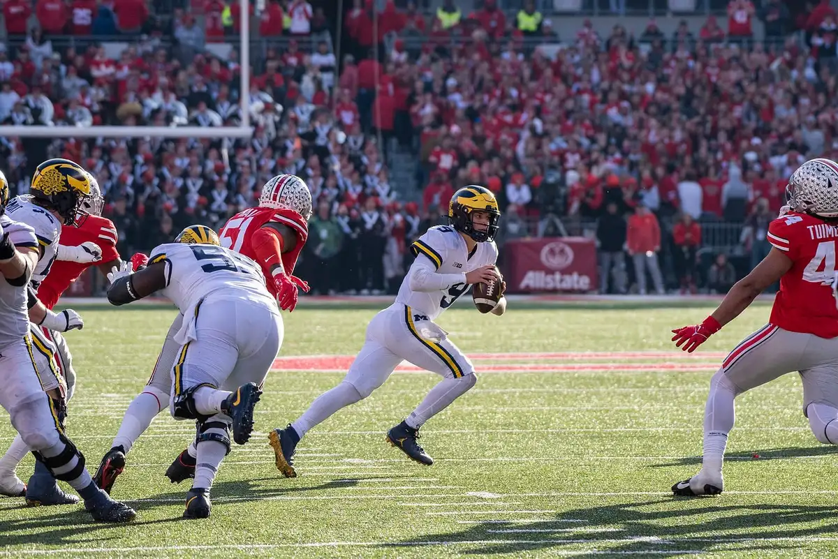 Ohio State defensive end J.T. Tuimoloau, number 44 in scarlet, closing from the edge on the Michigan quarterback as he moves out of the pocket at Ohio Stadium