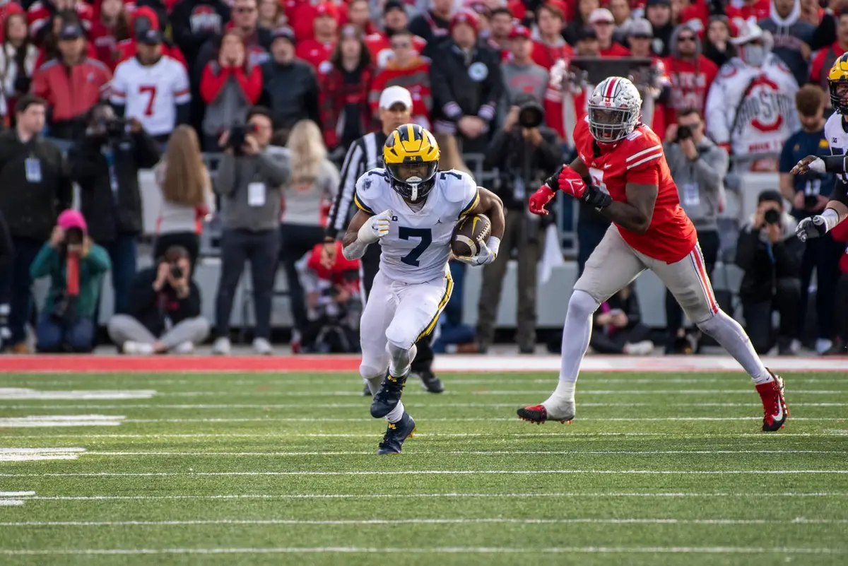 Ohio State defensive end Zach Harrison, number 9 in scarlet, closing in pursuit on a Michigan ball carrier in white along the sideline